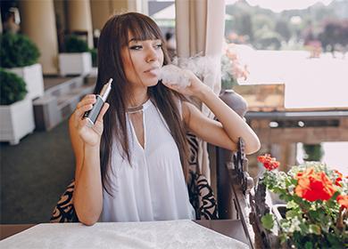 La jeune fille au café fume une cigarette électronique