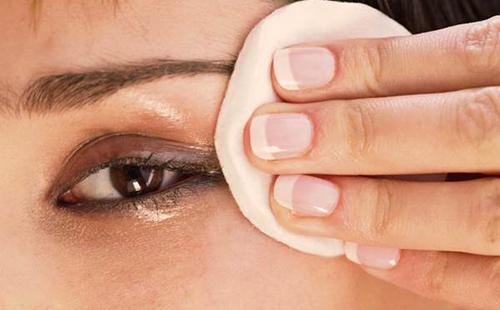 La belleza de ojos marrones se limpia los ojos con un algodón