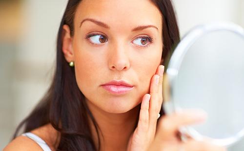 La jeune fille aux yeux bruns examine ses joues dans le miroir.