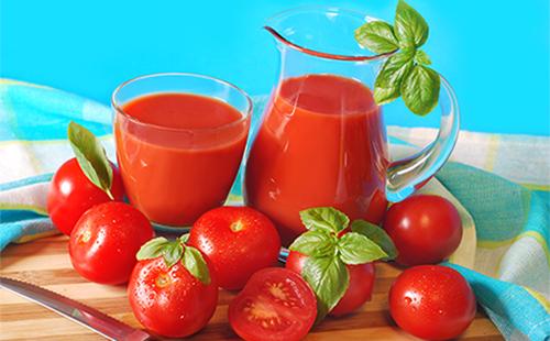 Tomatsaft i en kande og et glas, tomater og urter