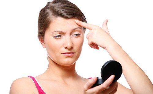 Femme examine le bouton dans le miroir