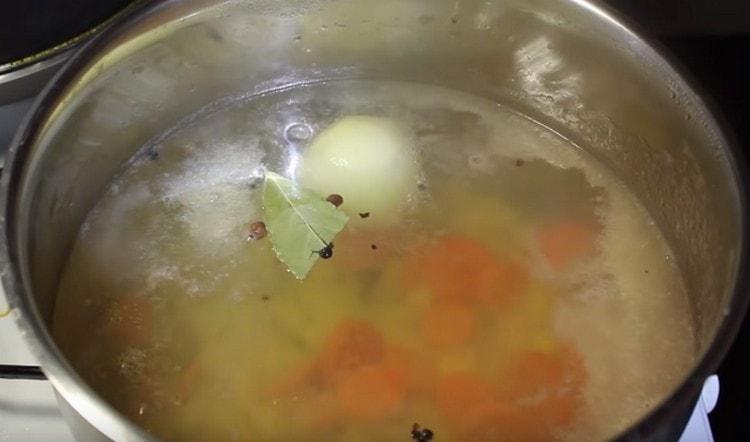 Adăugați ceapa întreagă în bulion, precum și frunzele de dafin și boabele de piper.