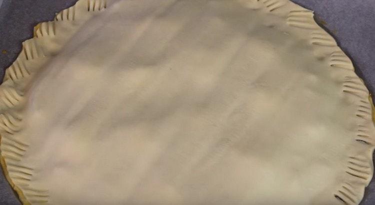 אנו מכסים את חומר העבודה ביריעה נוספת של בצק, לוחצים על הקצוות במזלג.