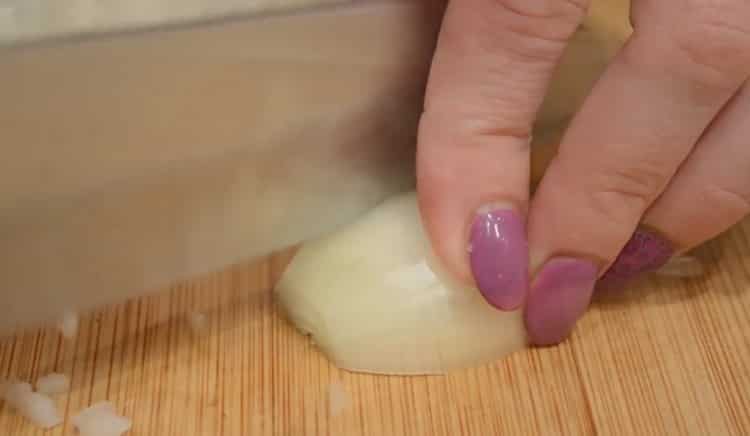 Hacken Sie die Zwiebel, um Koteletts mit Krabbenstäbchen zuzubereiten