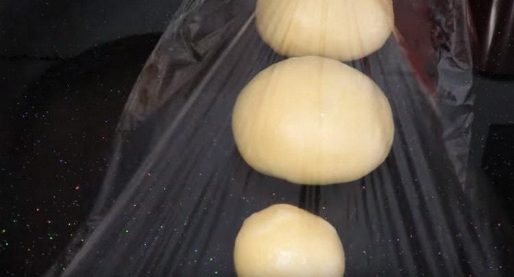 Vi delar upp den färdiga degen i 3 delar, var och en rullar i en boll och täcker i cirka 10 minuter med en film.
