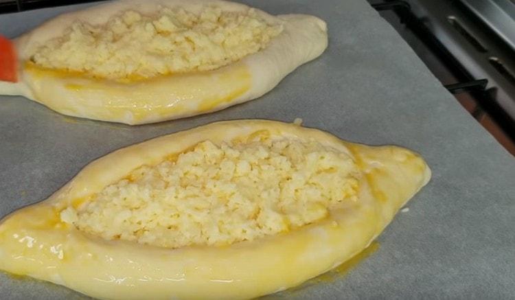 Прехвърляме лодките върху хартия за печене, покрита с пергамент, пълним ги с пълнеж и ги намазваме с яйце.