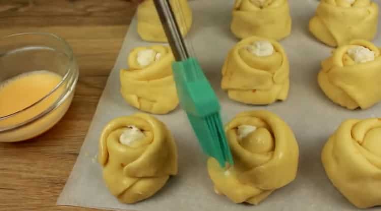 За да направите кифлички с извара от тесто с мая, намажете тестото с яйце