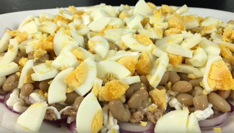 Schneiden Sie die gekochten Eier und verteilen Sie sie mit der nächsten Schicht Salat.