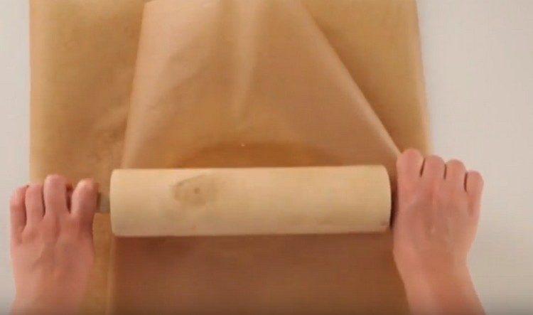 Vyjmeme těsto z ledničky a převálíme jej do tenké vrstvy mezi dvěma vrstvami pergamenu.