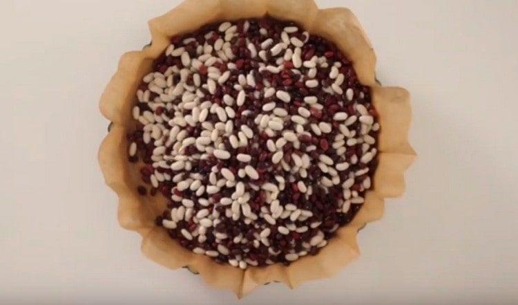 Polotovar přikryjeme pergamenem, nalijeme do něj fazole nebo cereálie, vložíme do trouby.