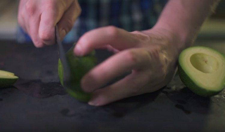 Tăiați blatul într-un avocado, astfel încât fructul să rămână constant pe foaia de copt.