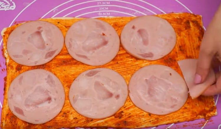 Pe aluat, întindeți cârnații fierti feliați.